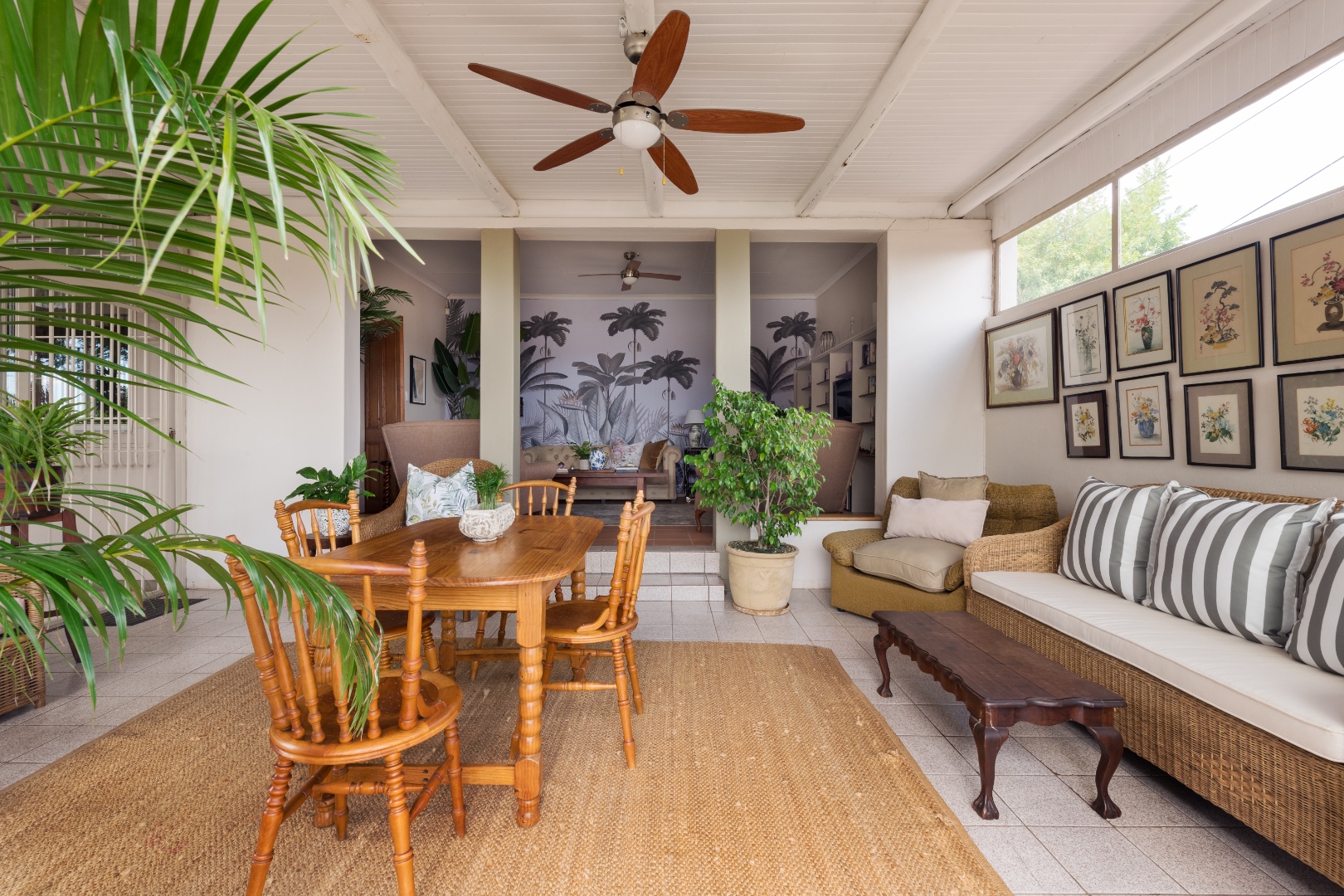 Covered sunroom with dining table, wicker lounge and tropical mural at House Falcon Guesthouse Pretoria